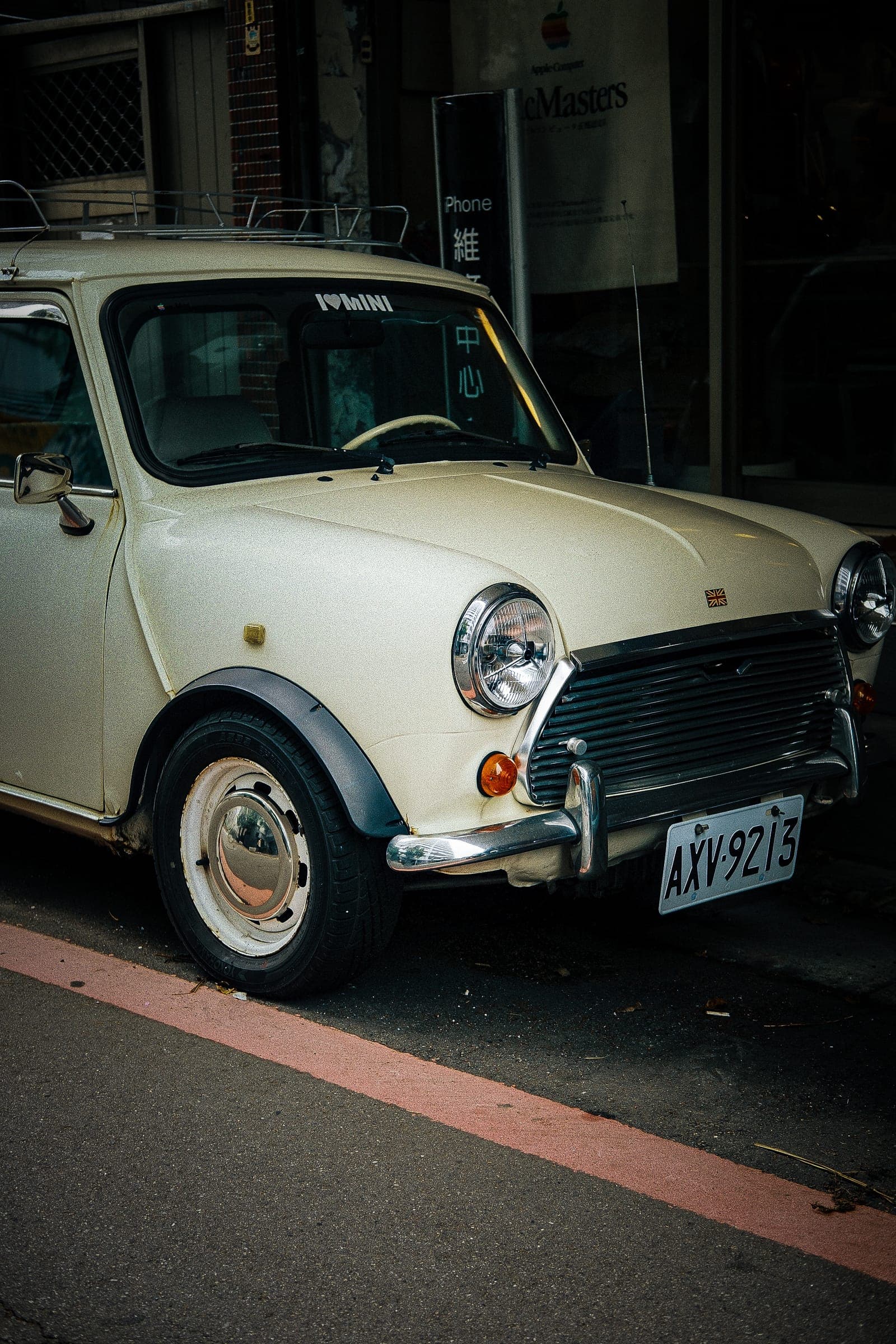 A cream classic Mini parked against a red-striped Taipei kerb.