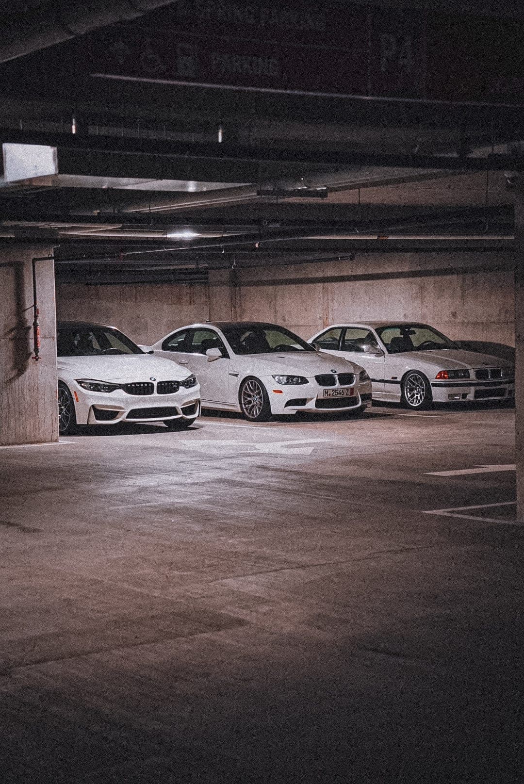Three white BMW M-series coupés parked together in an underground deck.