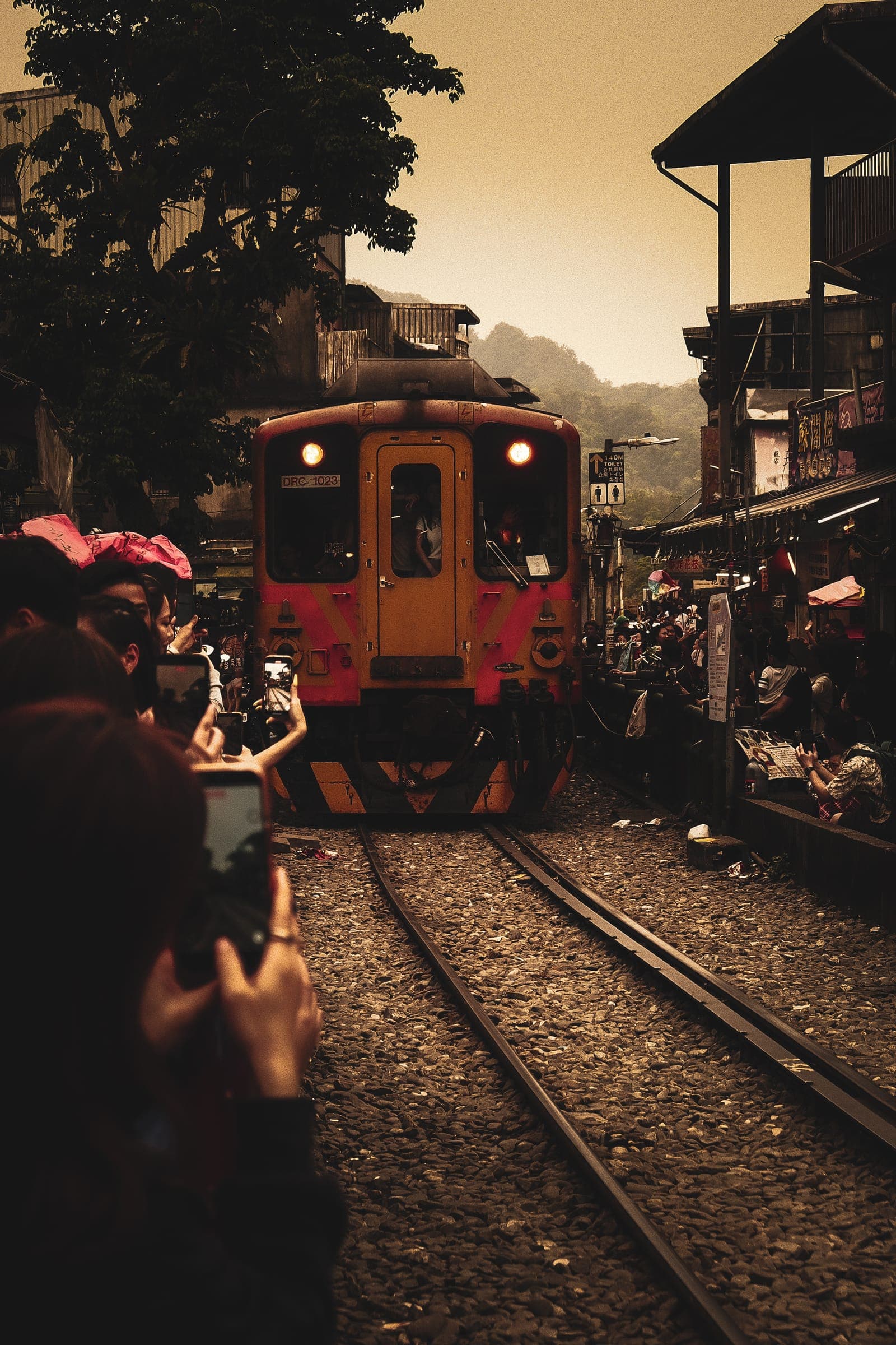 An orange local train arriving on the Pingxi line as visitors raise their phones.