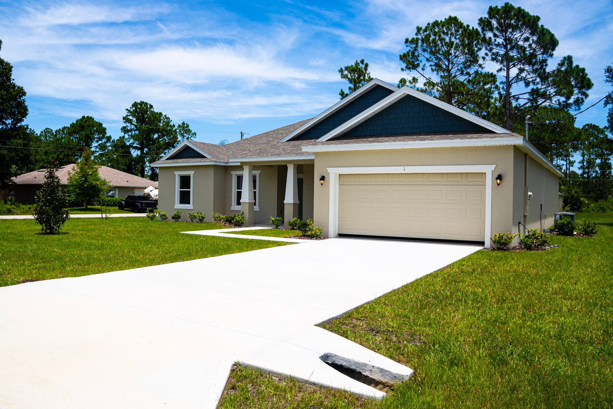 New single-family home with craftsman columns and twin blue-shake gables above a two-car garage, fresh sod and a wide concrete driveway in the foreground.