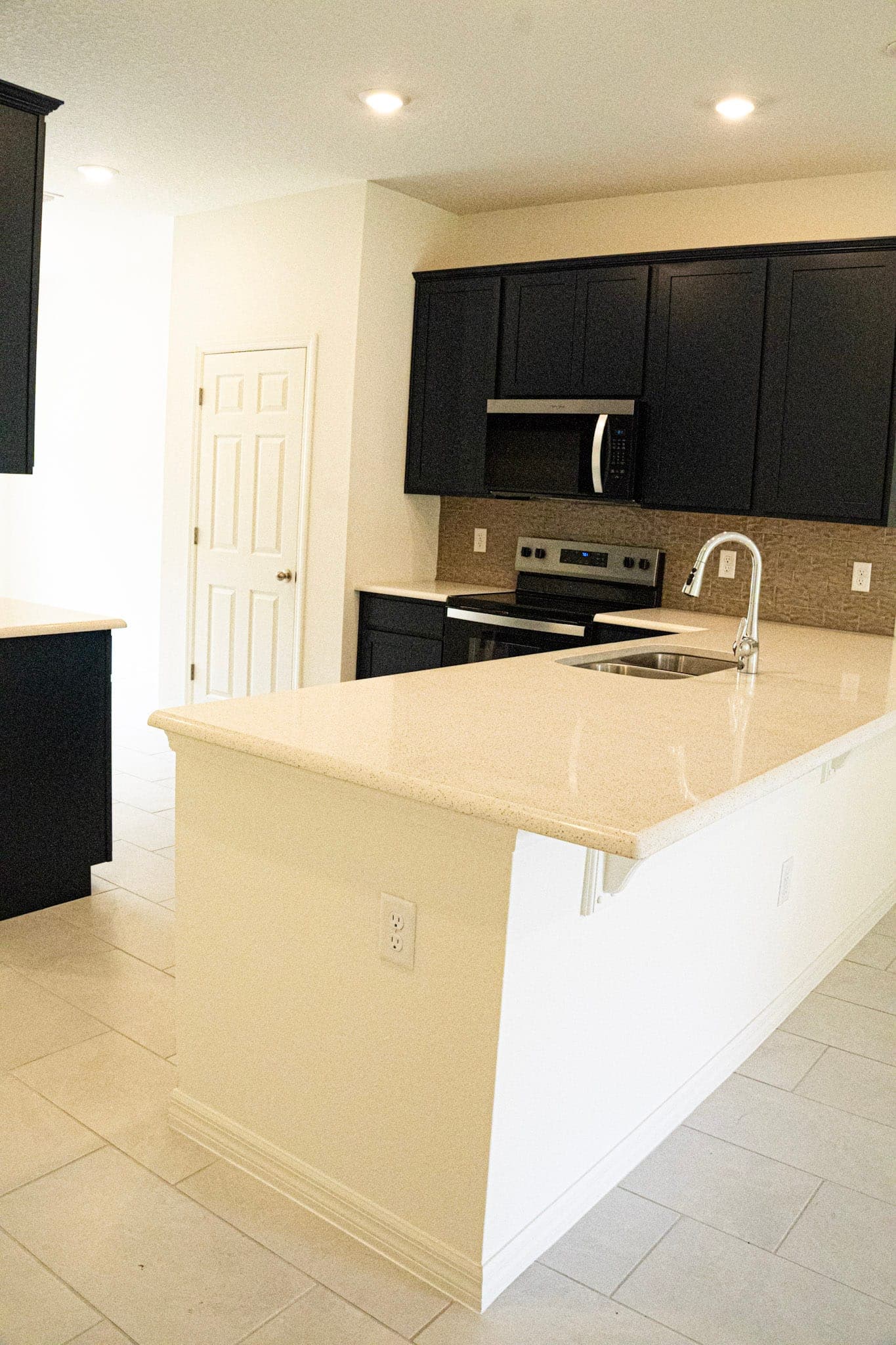 Kitchen island with cream quartz counter and white panel base against espresso shaker cabinets and tile floor.