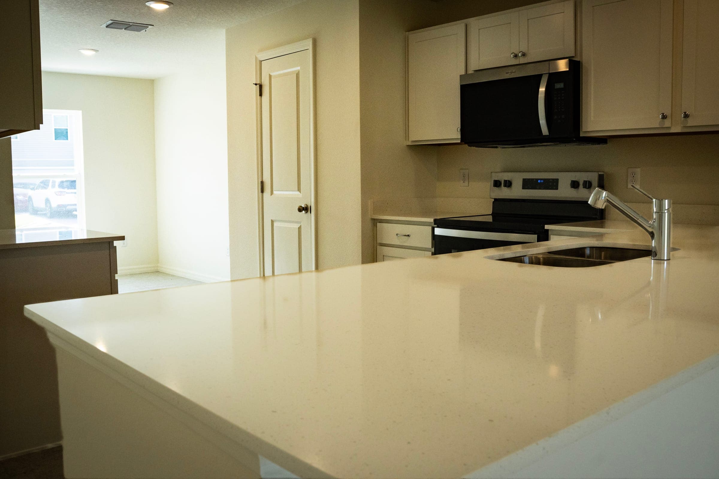 Low angle across a quartz breakfast bar toward white shaker cabinets, stainless range, and a pantry door.